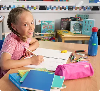 Menina na escola sentada à secretária a escrever com um lápis etiquetado, rodeada por outros artigos escoLares de idosos etiquetados