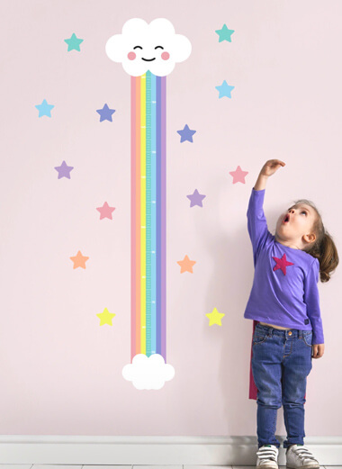My Nametags gráfico de altura de nuvem de arco-íris em uma parede rosa com uma garotinha ao lado